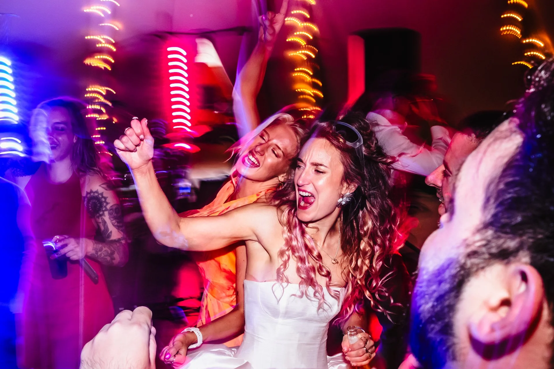 People dancing and celebrating at a party with colorful lights and a lively atmosphere.