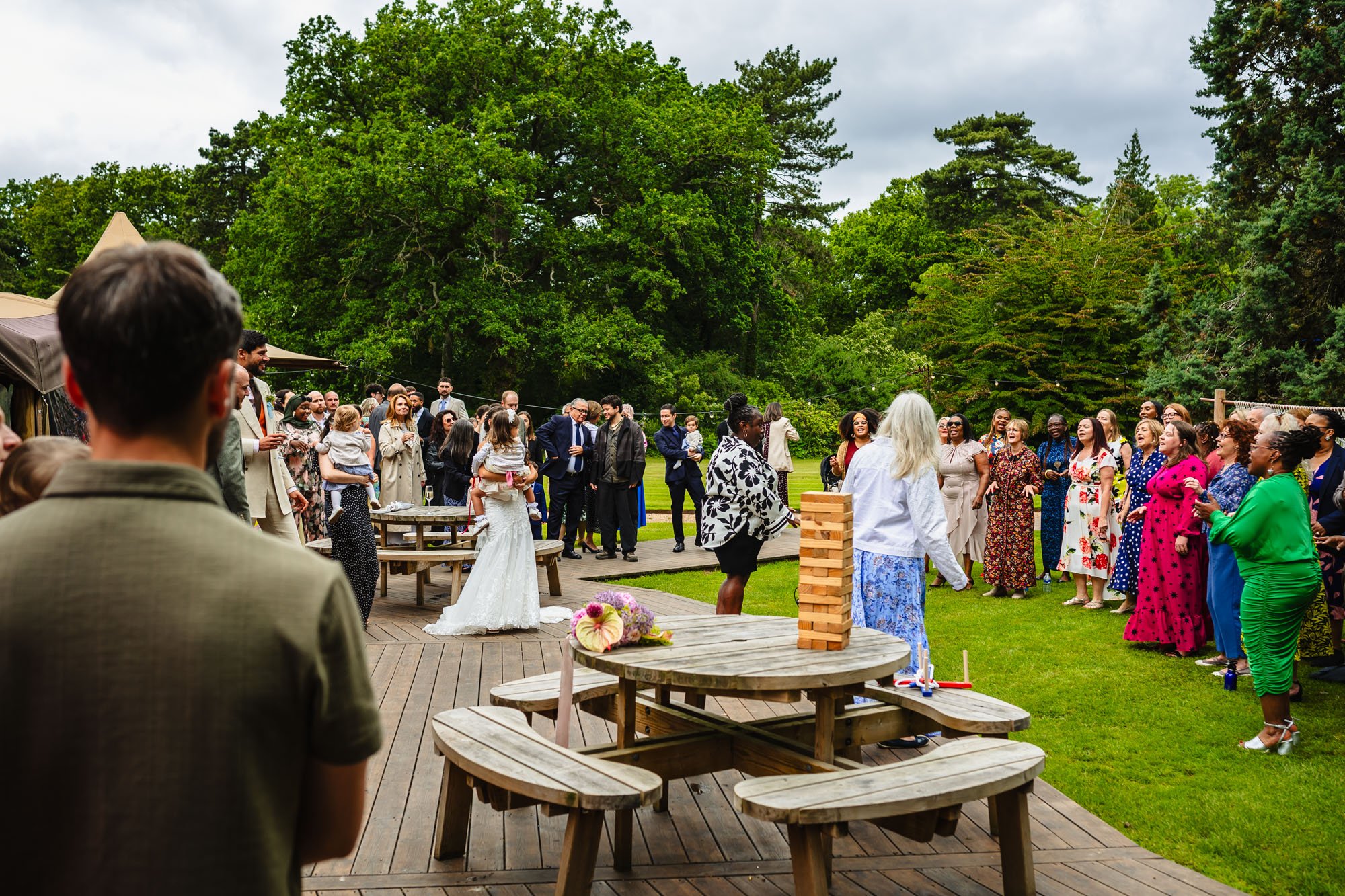 wide photograph of a wedding reception on the lawn at tipis at whatton house. To the right is a gospel choir, singing for the guests on the left.