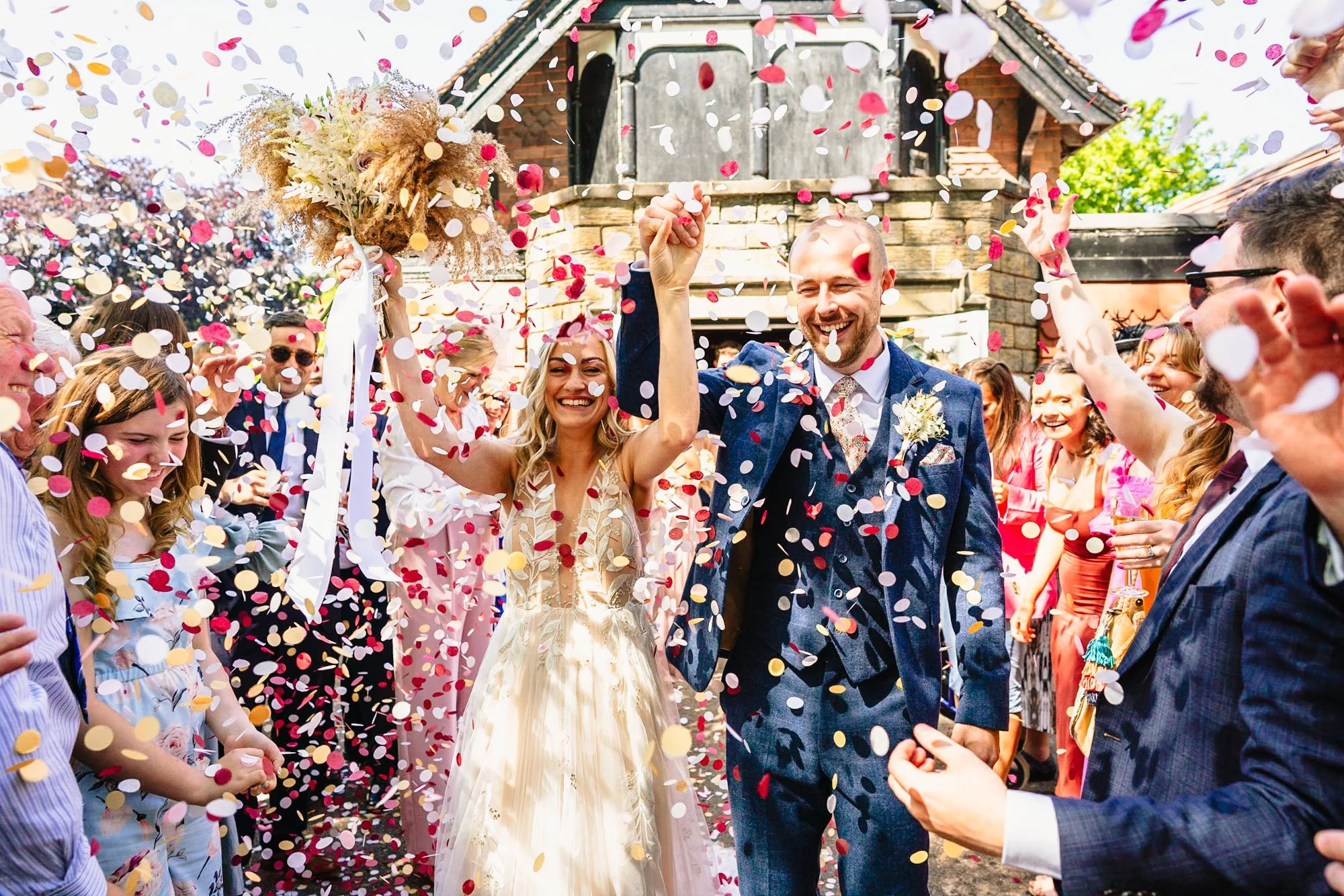 photograph of a bride and groom walking through a huge amount of confetti  with big smiles on their faces
