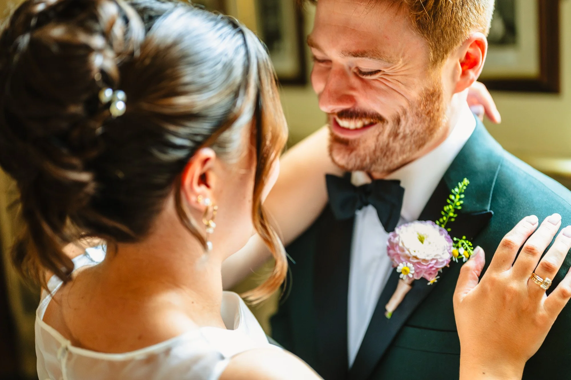 Close up image of a man smiling at a woman. He is wearing a green suit with a floral buttonhole.