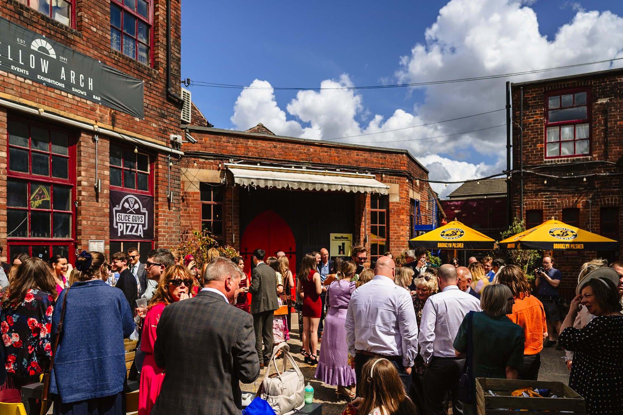Photo of the exterior of Yellow Arch studios with wedding guests standing outside during the reception. Included as part of a list of sustainable wedding venues.