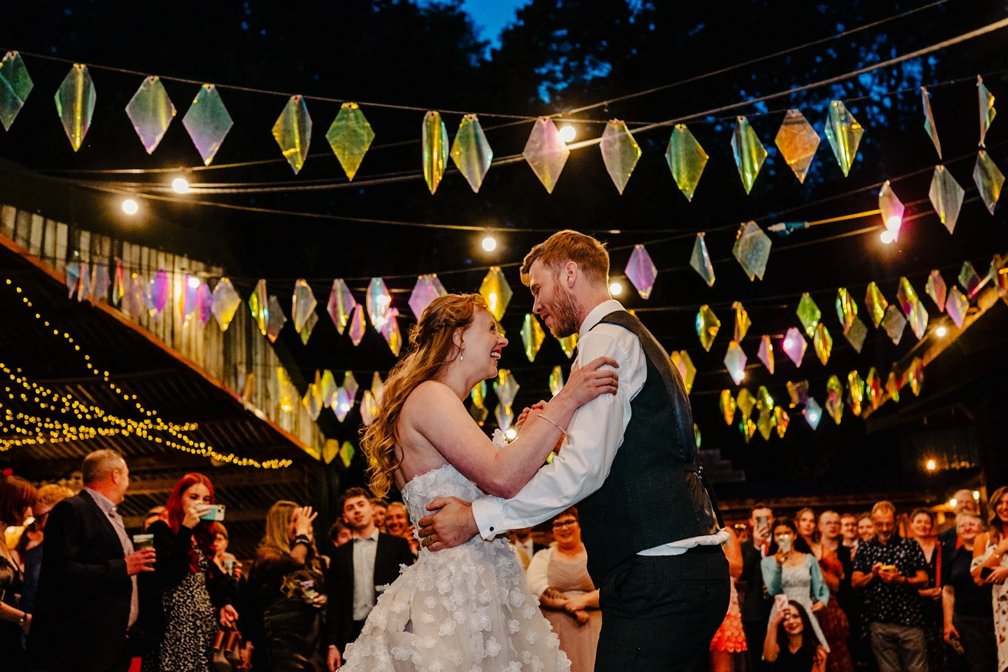 photograph of a bride and groom smiling and dancing outdoors under reflective bunting at Whitebottom Farm in Stockport by natural wedding photographer Caroline Goosey