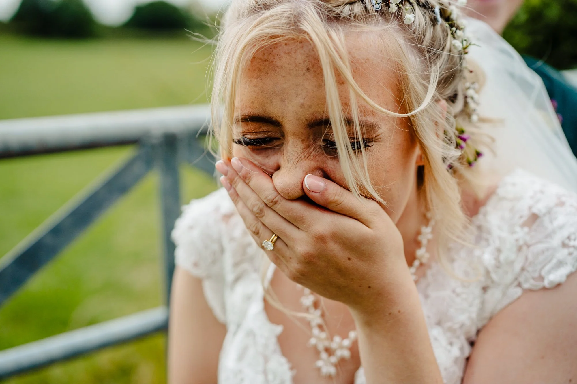 Close up photograph of a bride laughing. She is outdoors with a farm gate behind her.