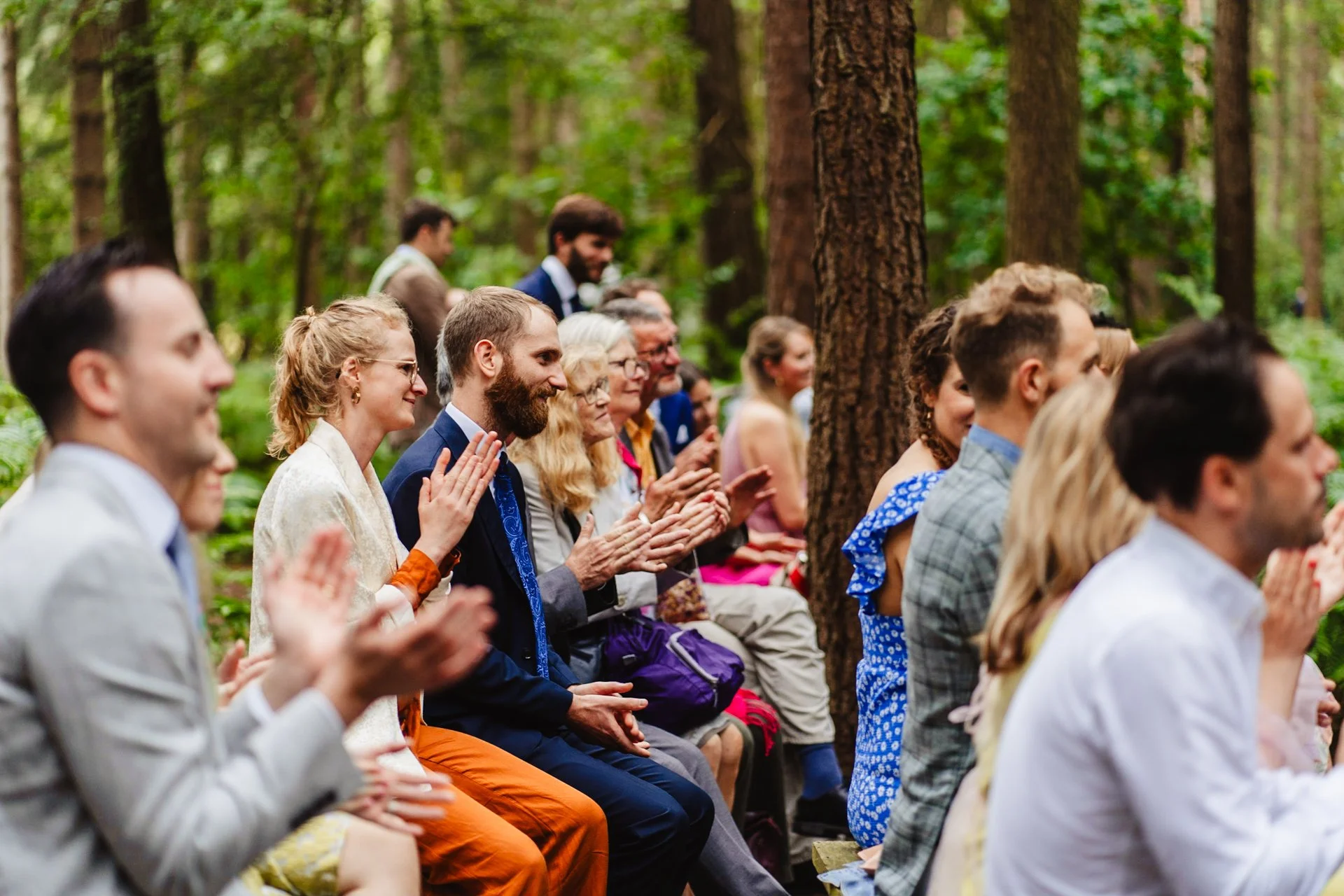 Photograph of guests applauding during an outdoor woodland wedding reception at Camp Katur in Northumberland.