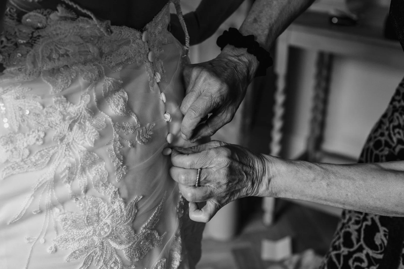 black and white photograph of an older woman's hands as she buttons up the back of her daughter's wedding dress by documentary wedding photographer Caroline Goosey