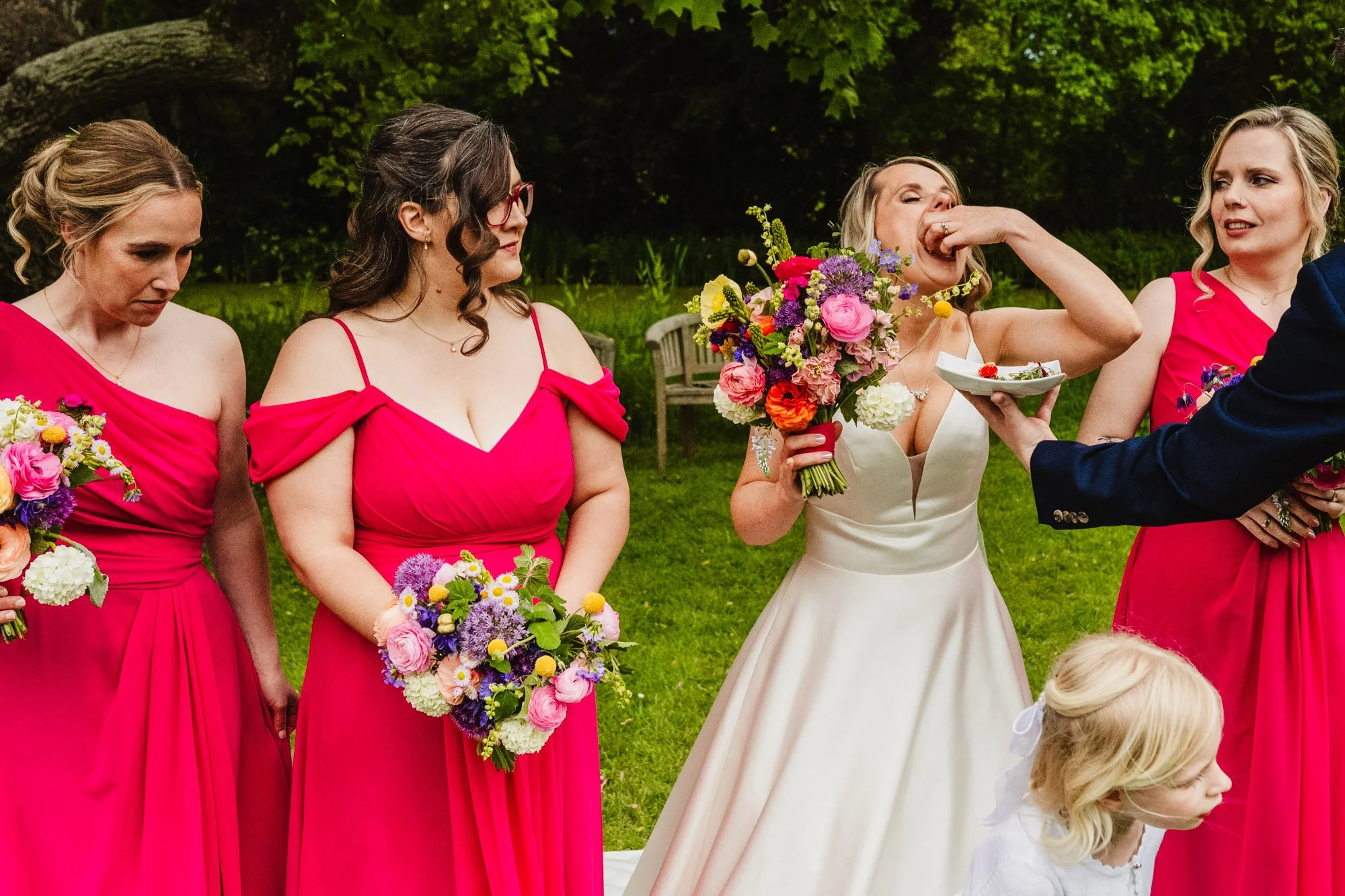 Photograph of a bride eating a canape while her bridesmaids react with various expressions.