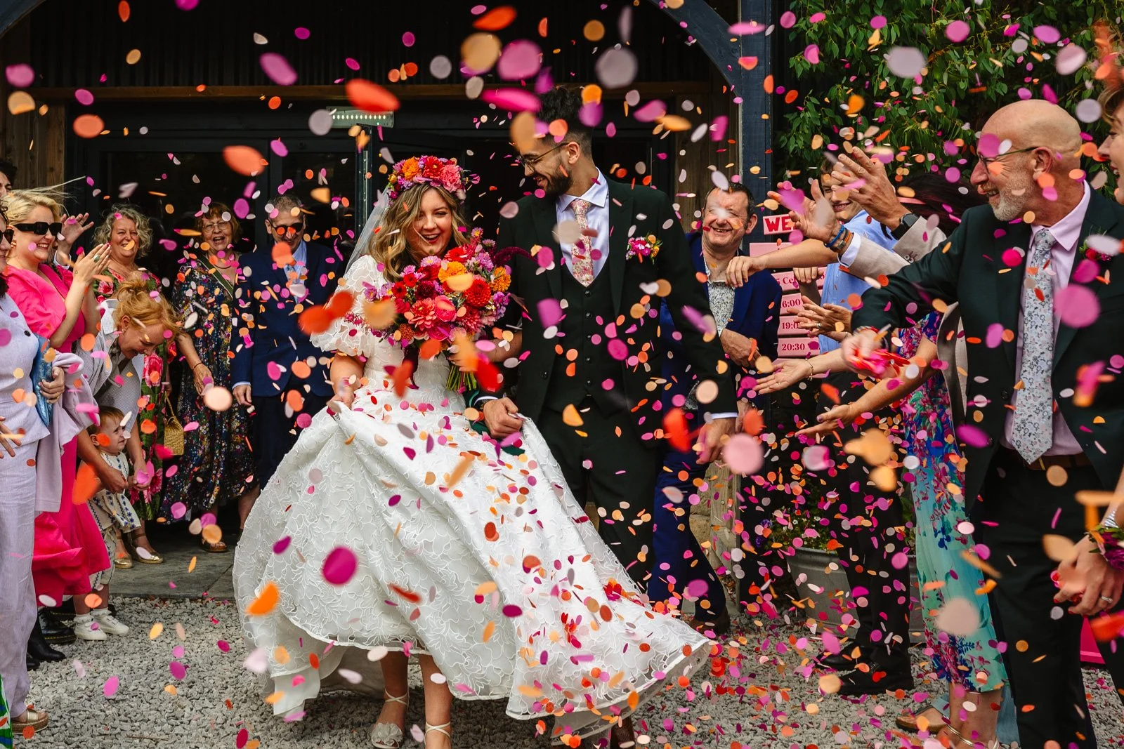 Bride and Groom exit their ceremony at Peak District Holiday Barn to a cloud of colourful confetti being thrown by their guests