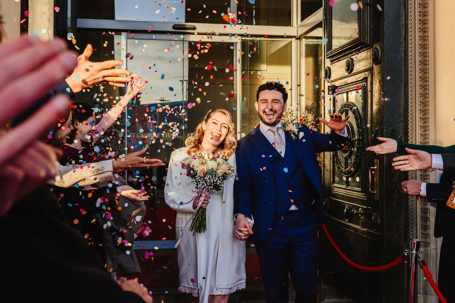 A man and a woman exit St George's Hall - the registry office in Liverpool - after their wedding. They are showered with colourful paper confetti.