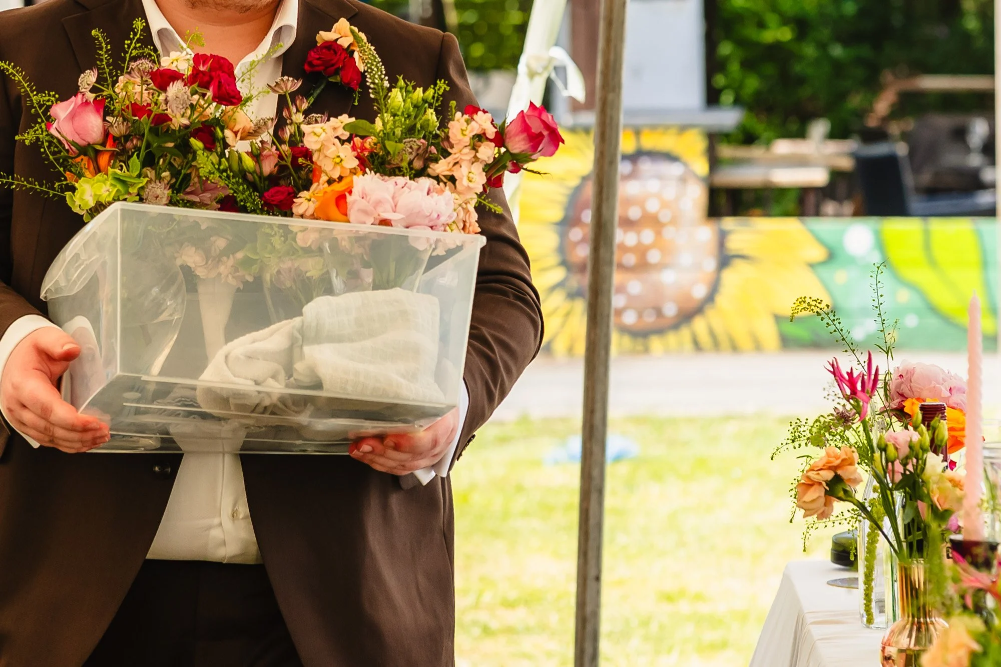 a groomsman carries a box of flowers to place on tables during a wedding reception