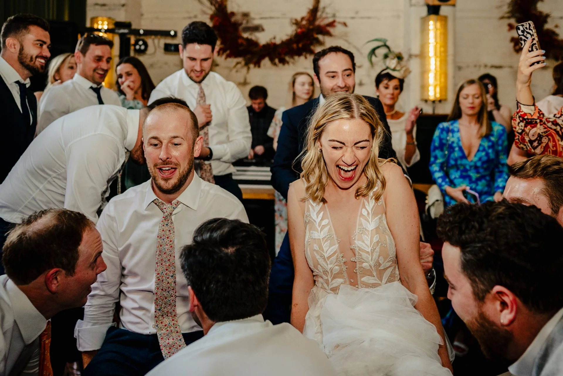 A couple sit on chairs on their dancefloor, waiting to be lifted by their guests. The groom looks nervous, the bride is shrieking. Wedding at The Mowbray in sheffield.