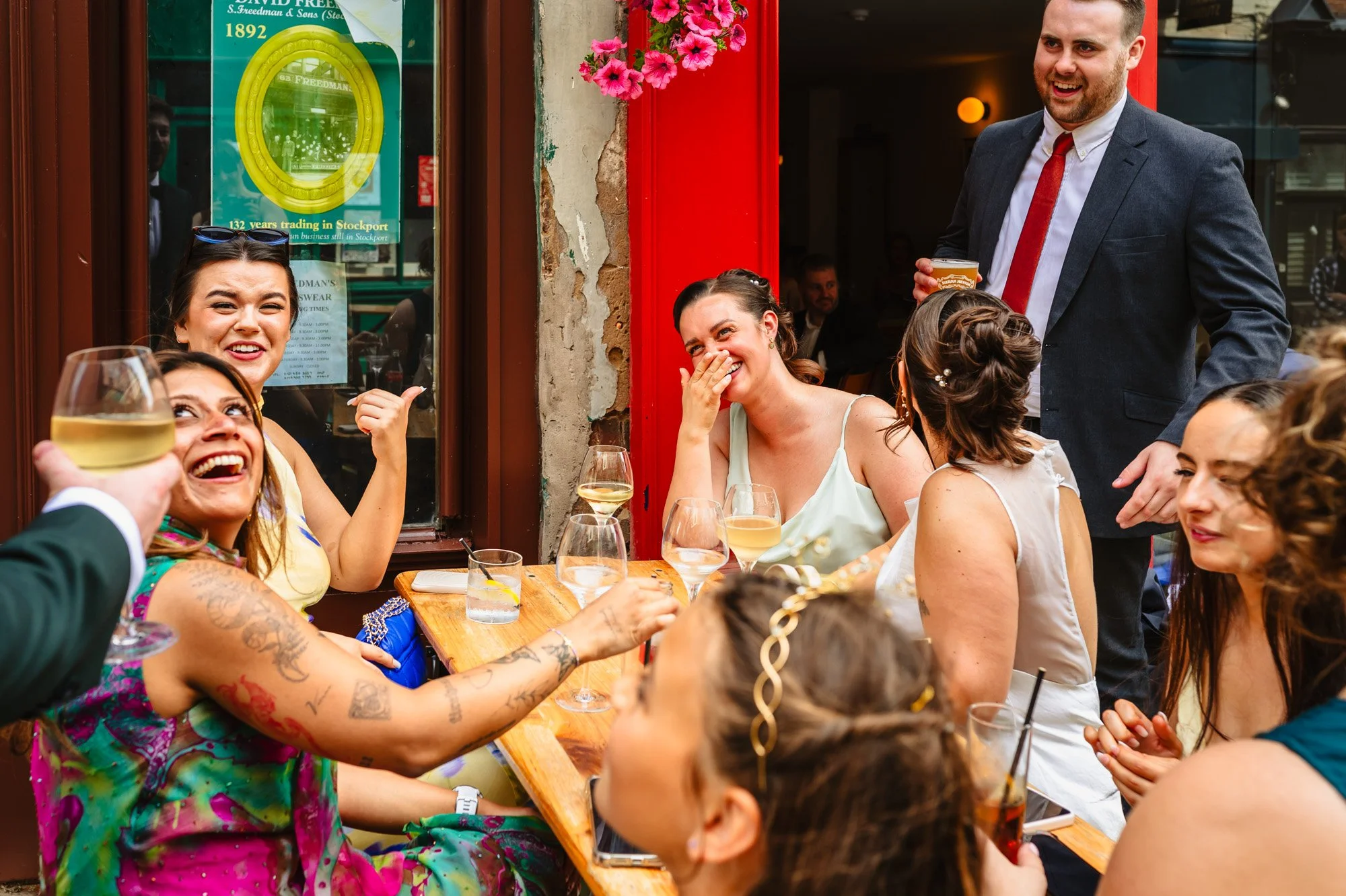 Candid style photograph of wedding guests at a table. They are interacting with each other and lauhing.