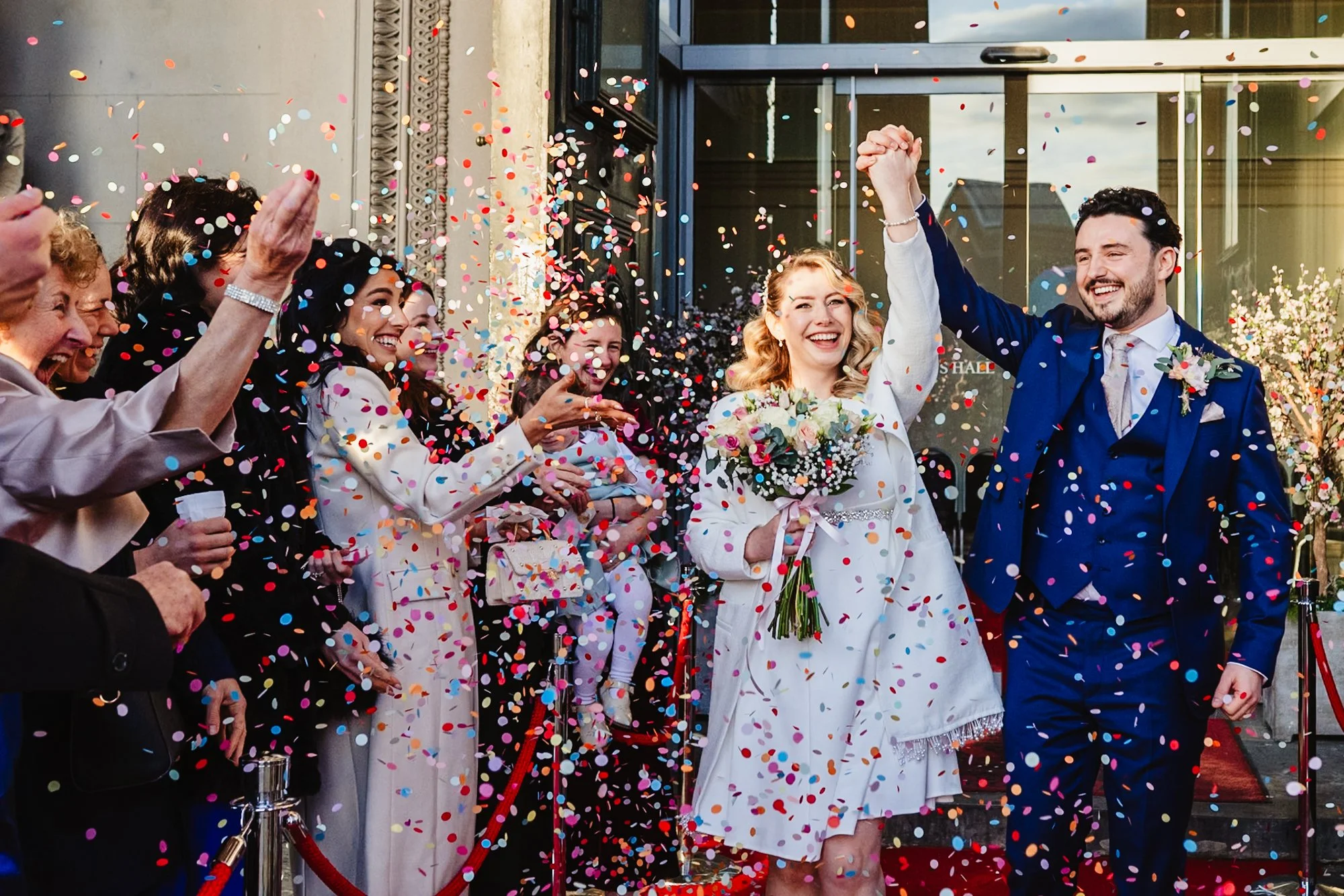 A photograph of a couple exiting their wedding ceremony at St George's Hall in Liverpool to a cloud of colourful confetti