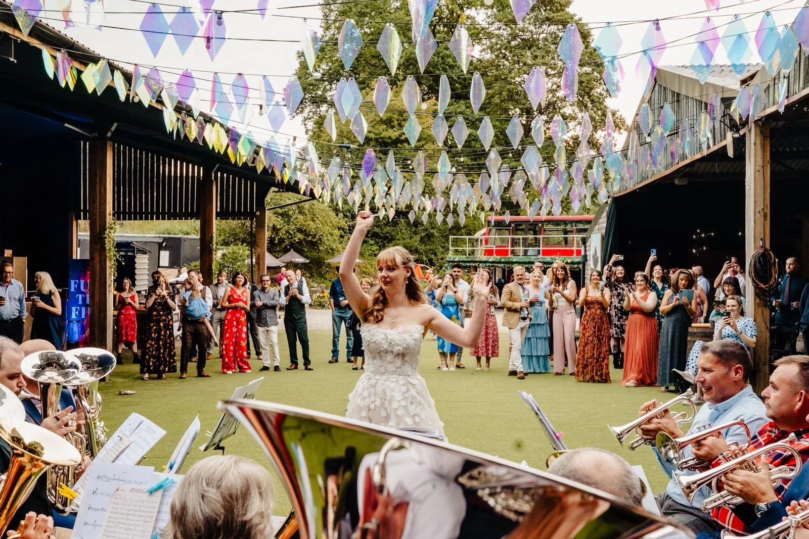A bride in a wedding dress conducts a brass band outside on a farm at a wedding venue in Stockport.