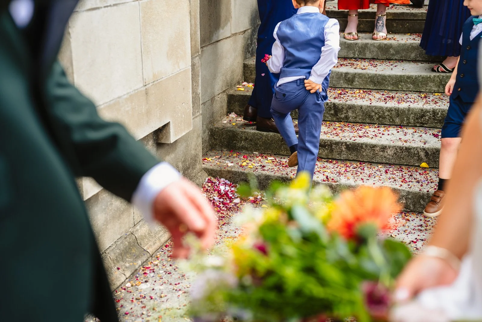 Photo of a little boy in a suit scratching his bum while he walks up some steps. Confetti is all around him on the ground.