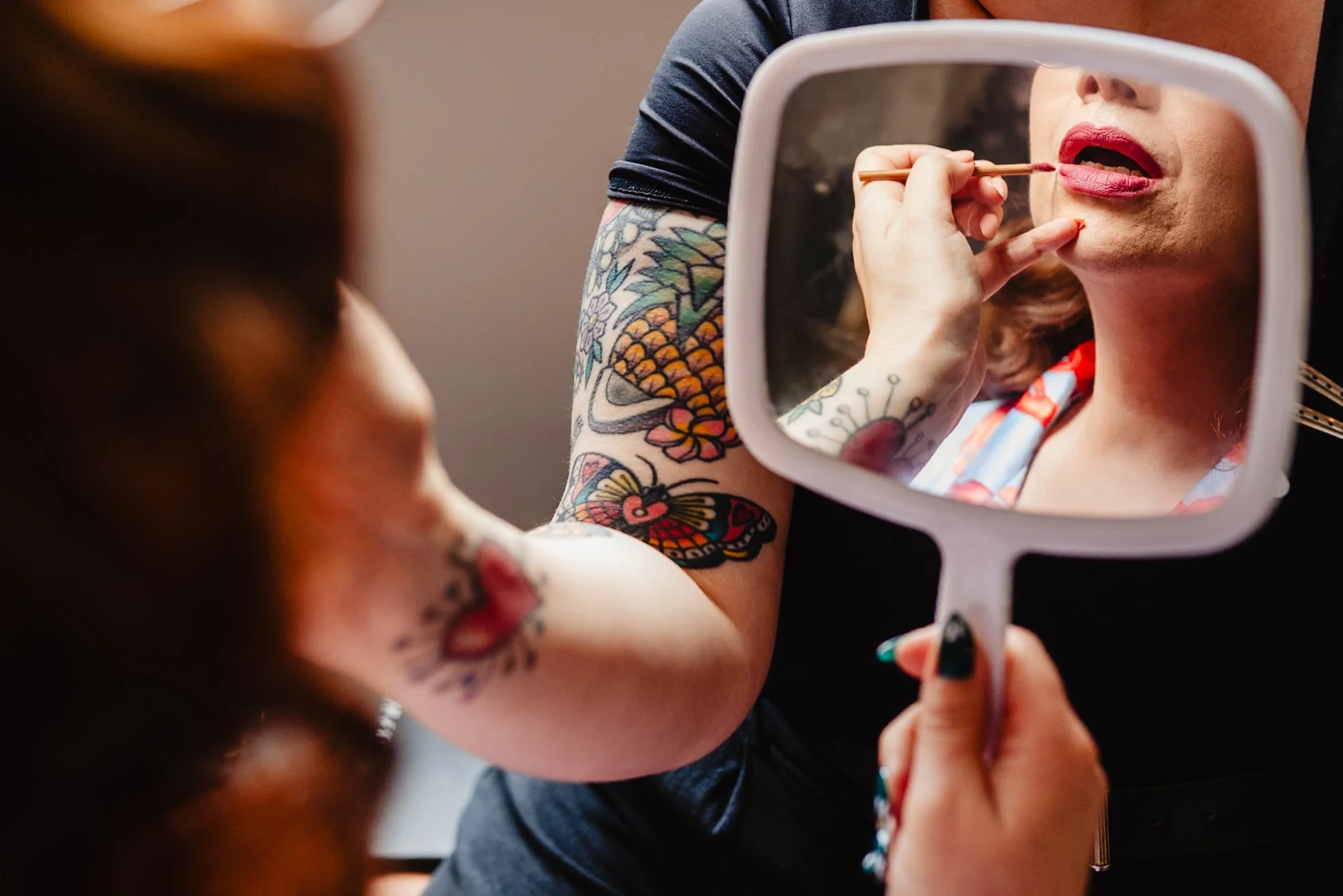 Photograph of a woman having her makeup applied on her wedding morning in Manchester. The lower part of her face is visible in a mirror.