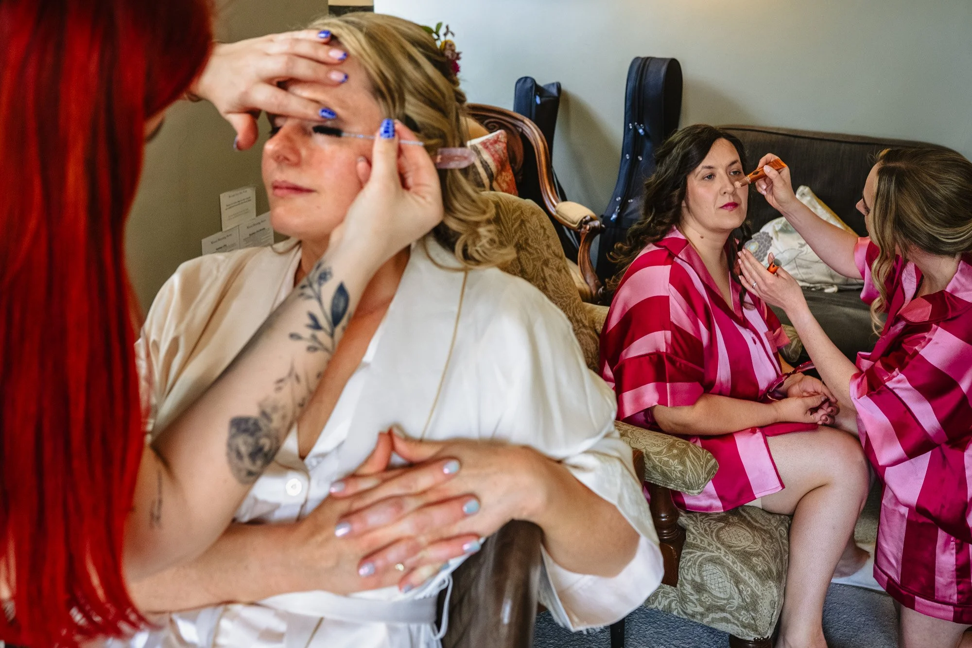 photograph of a bride having her makeup done in the foreground while two bridesmaids in matching pjs do theirs in the background
