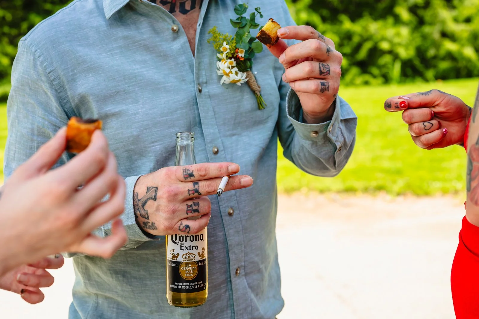 close up photograph of a man holding a lit cigarette, bottle of Corona lager and a fondant potato during a wedding reception at Duddon Mill Farm by documentary photographer Caroline Goosey