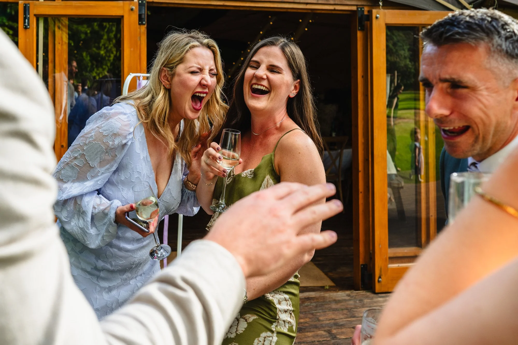 two female wedding guests laugh heartily at a wedding at the tipis at whatton house by documentary photographer Caroline Goosey