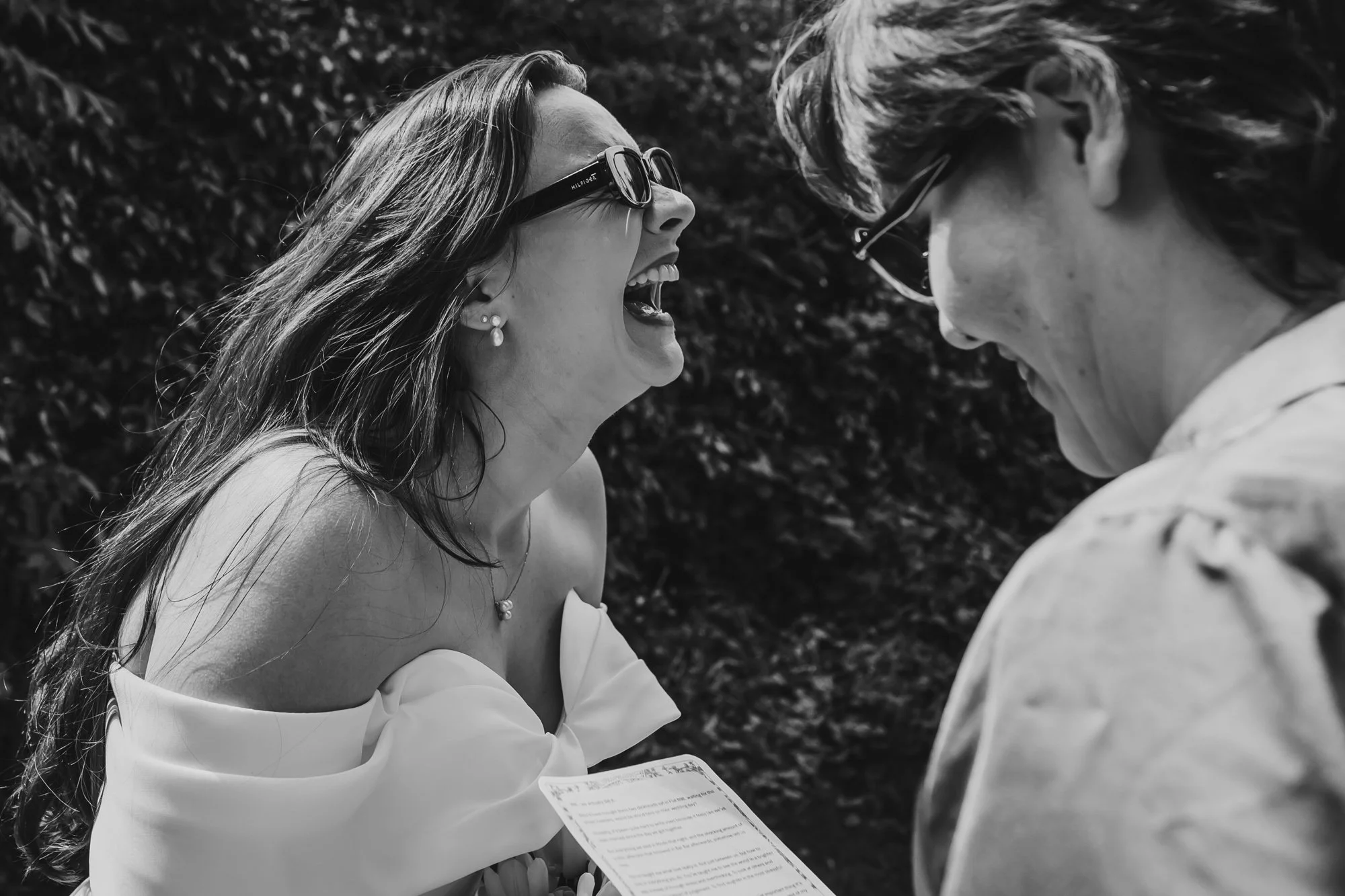 black and white close up photograph of two women laughing together outside at Lost, a Cheshire wedding venue, after just getting married there.