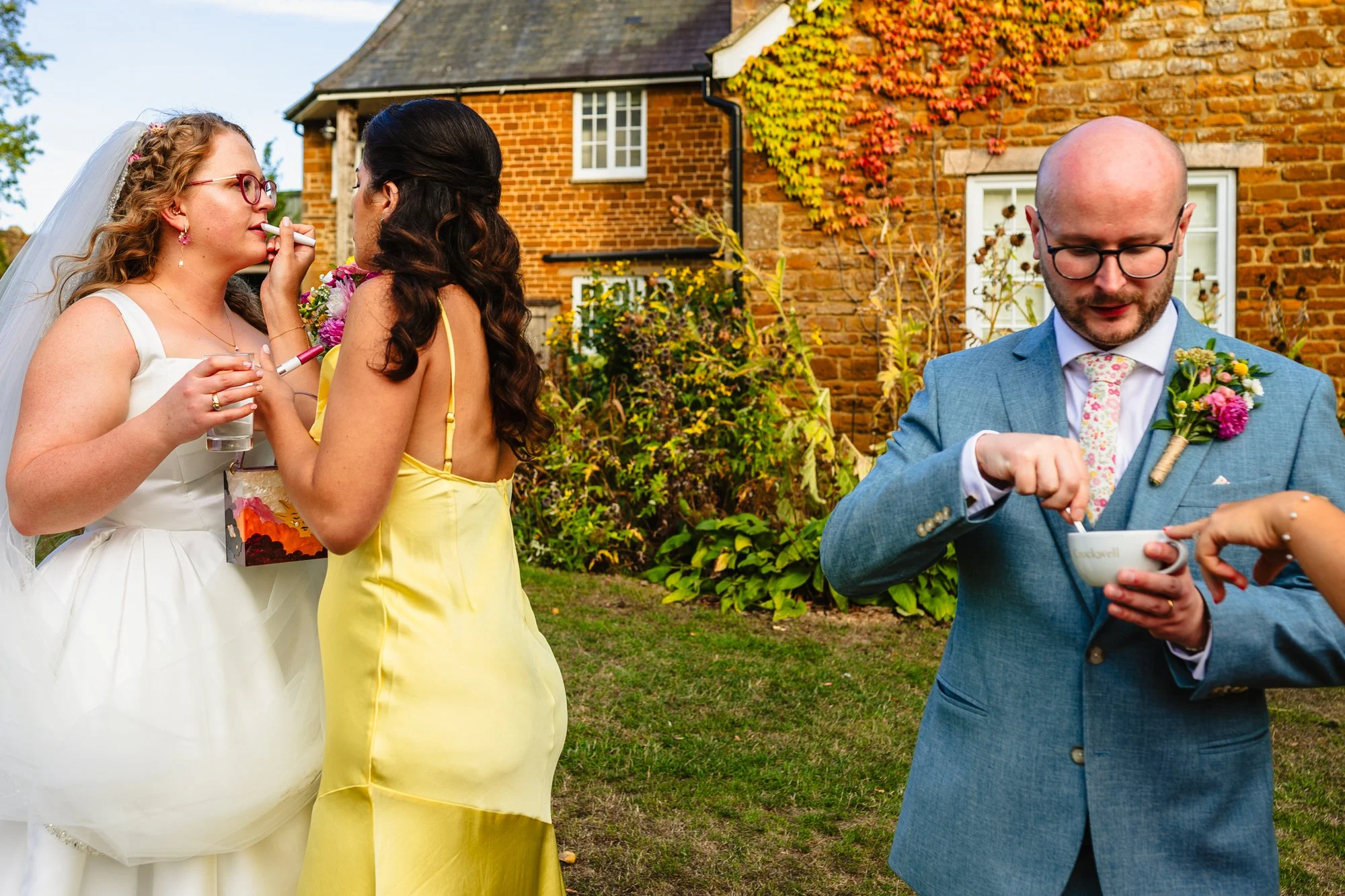 A bridesmaid tops up a bride's lipstick while a groom drinks a coffee
