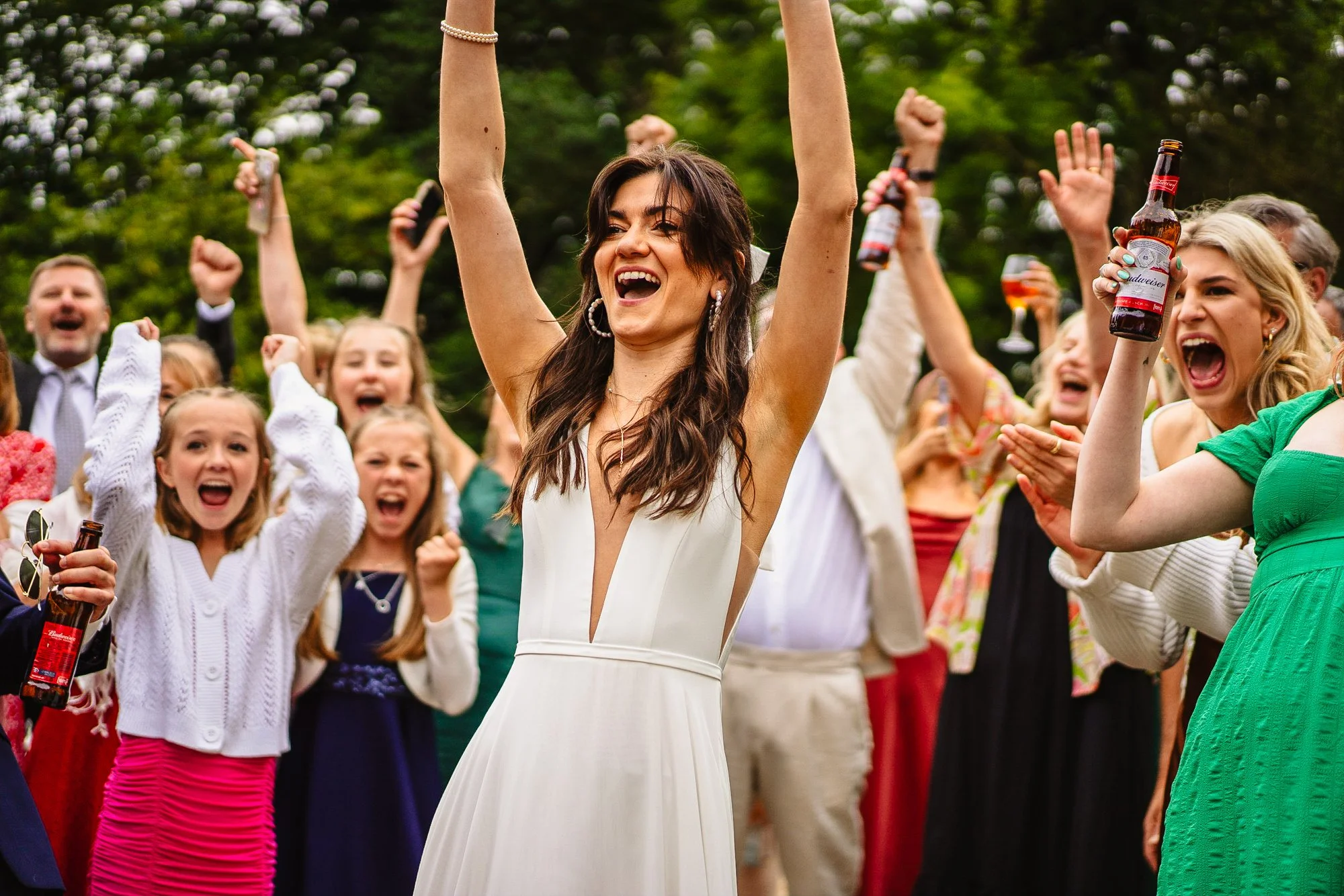 photograph of a bride cheering surrounded by other wedding guests also cheering with arms in the air