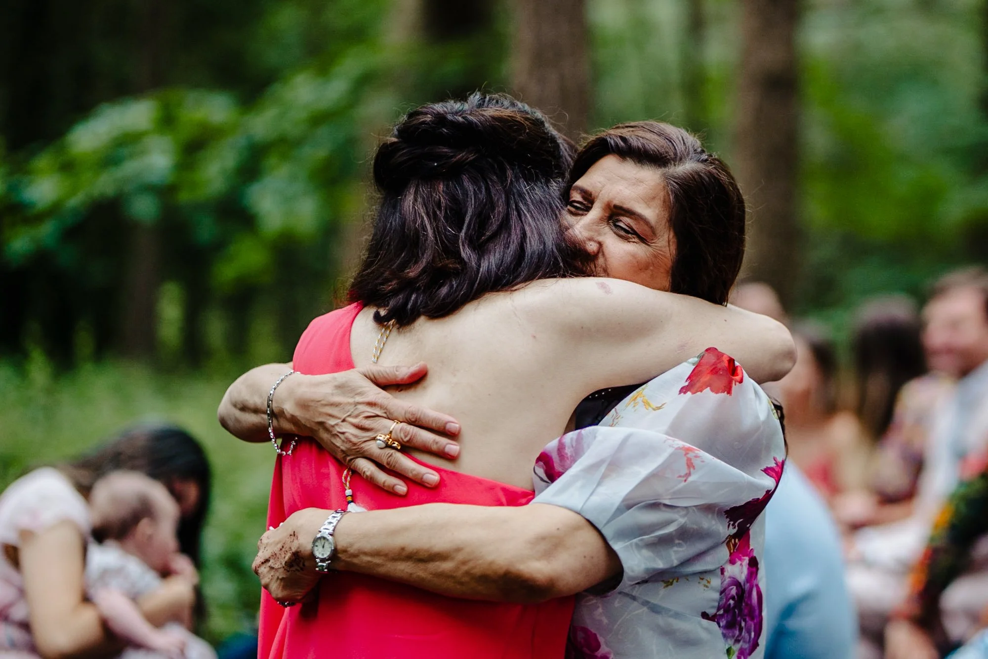 Candid wedding photograph of two women hugging in the woodland wedding space outdoors at Camp Katur in Northumberland