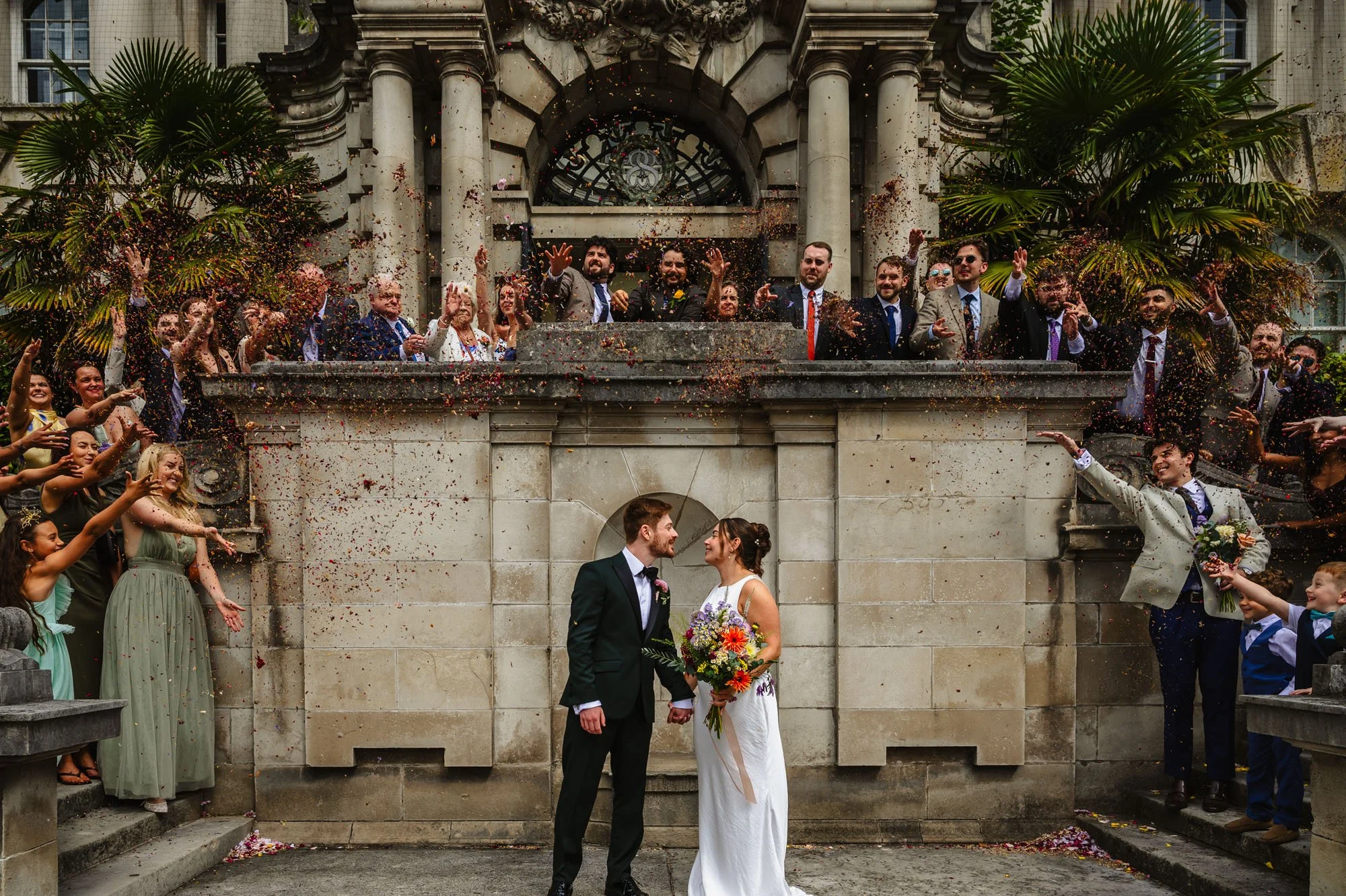 Photograph of a wedding party throwing confetti on a bride and groom outside Stockport Town Hall
