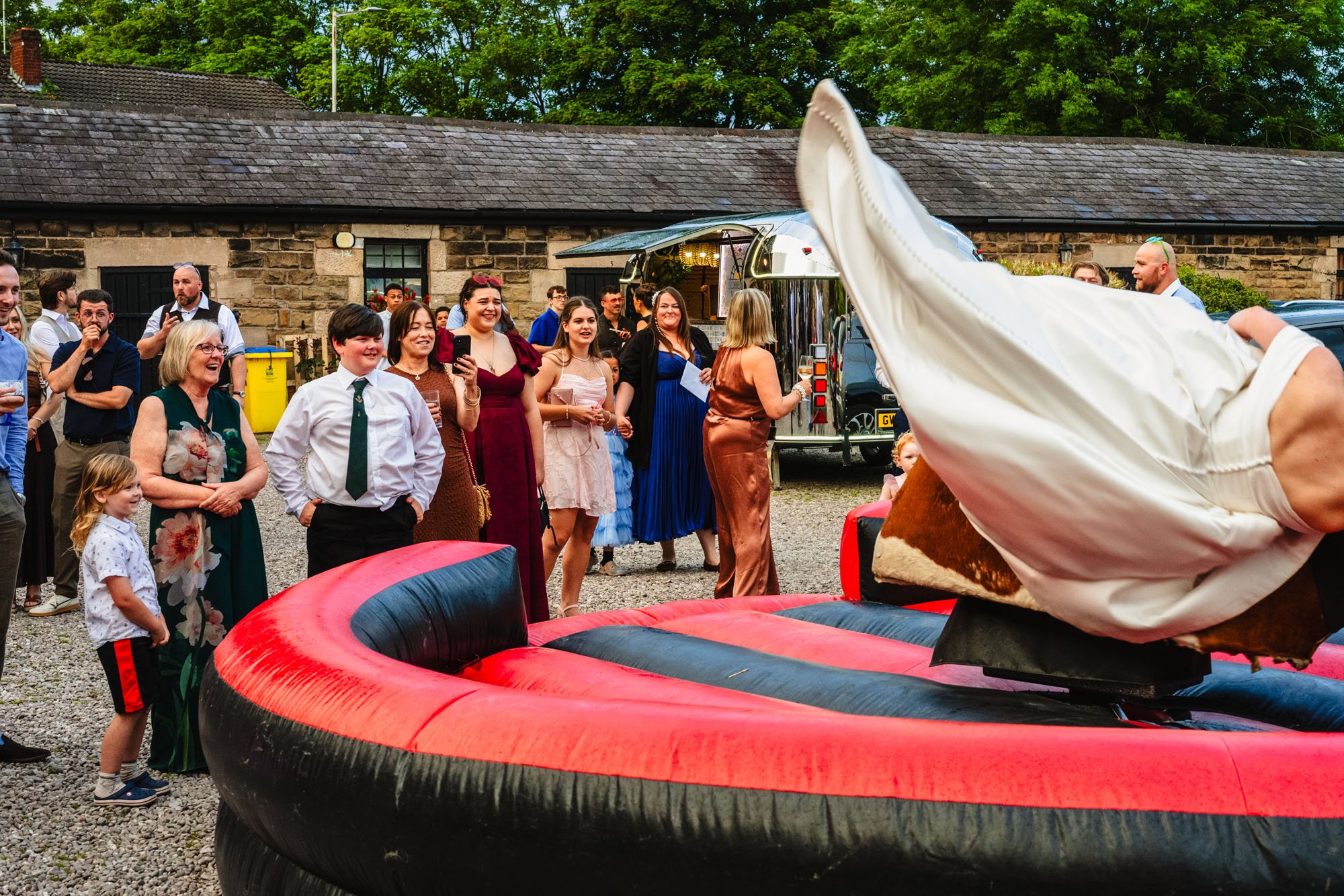 photograph of a bride falling from a rodeo bull while wedding guests look on. The photo was taken outside at Lost on the Wirral.