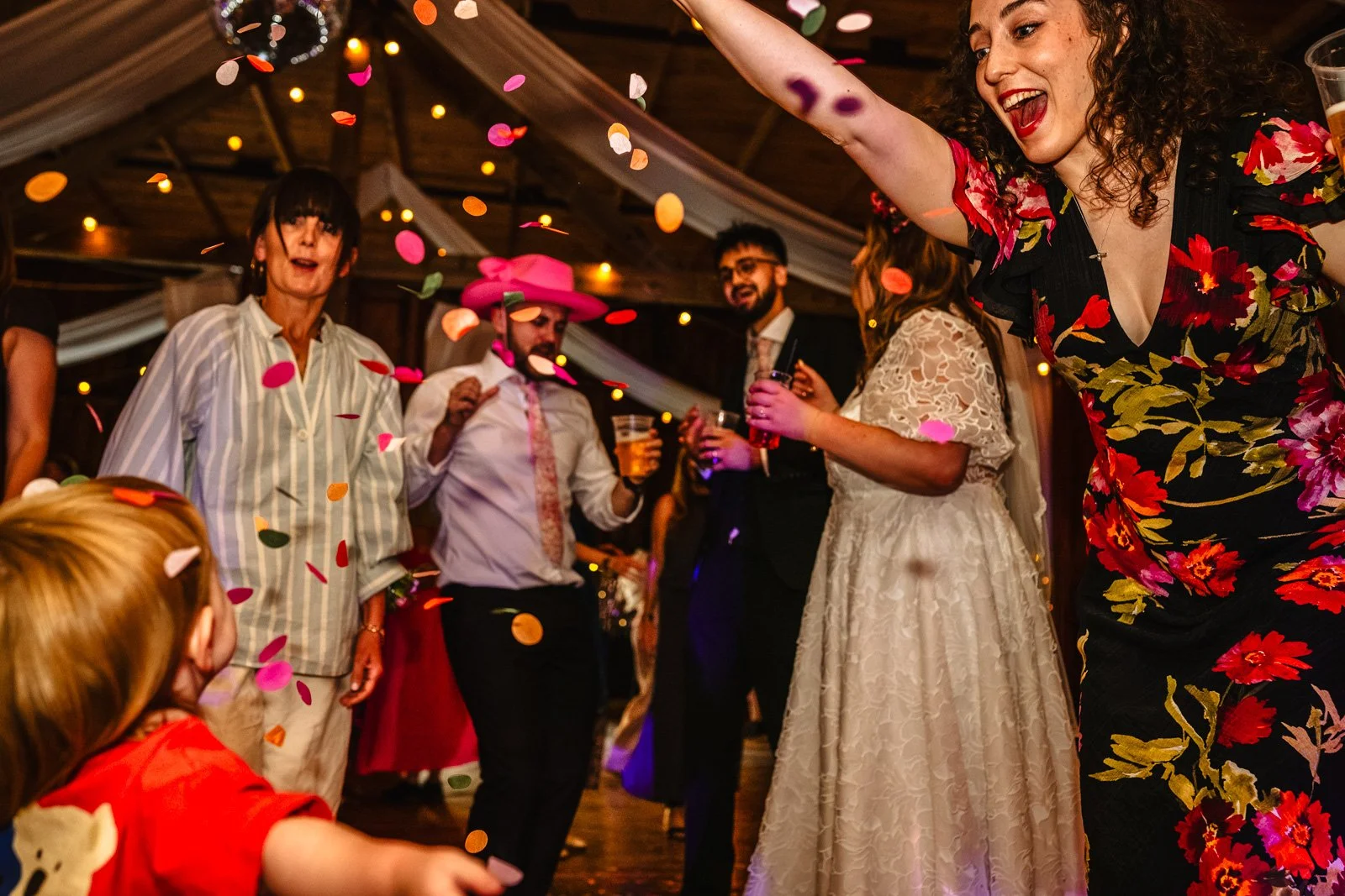A young woman scatters confetti from a height over a toddler on the dancefloor
