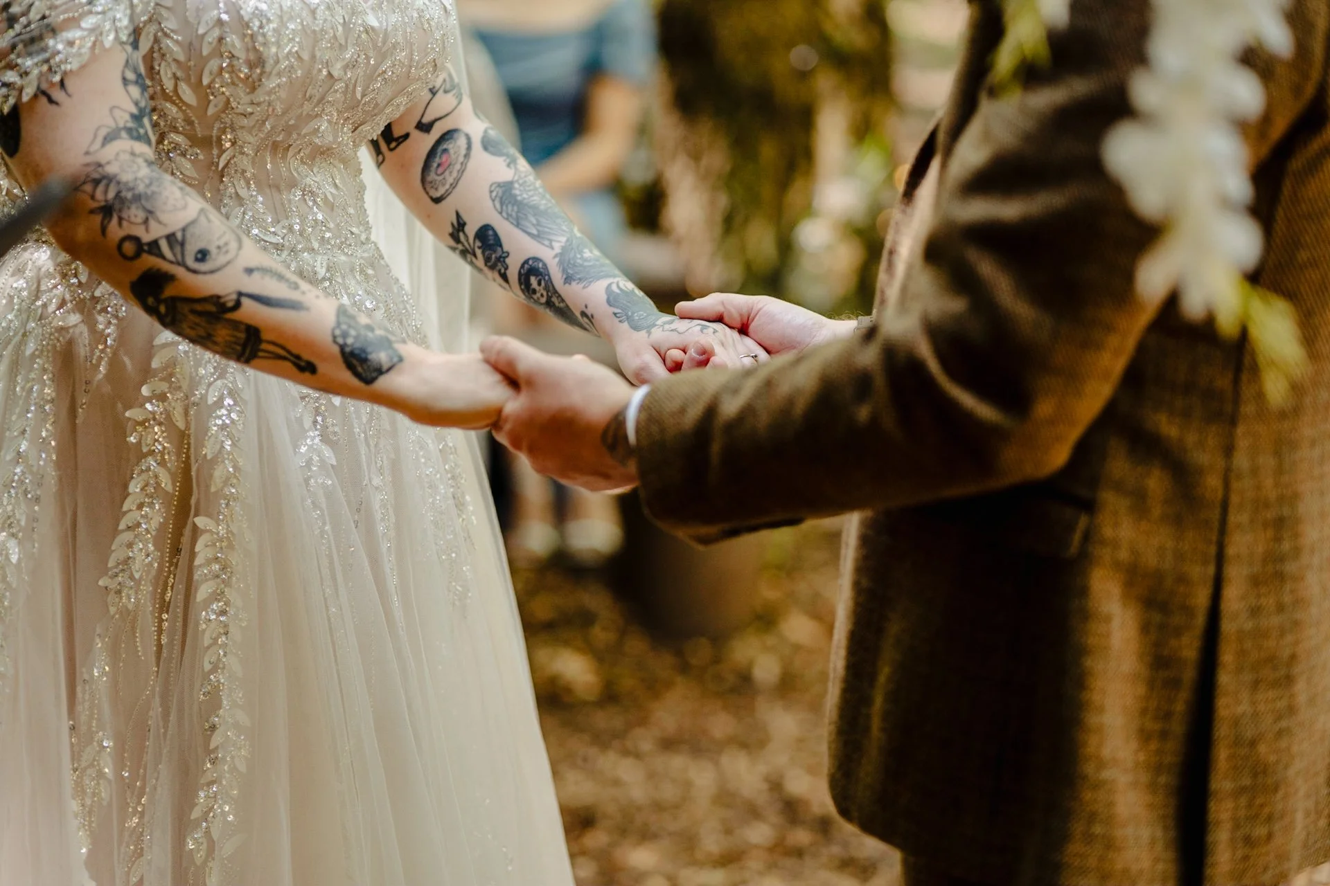 Photograph of a tattooed bride and groom holding hands at their outdoor wedding ceremony at Cheshire Woodland Weddings