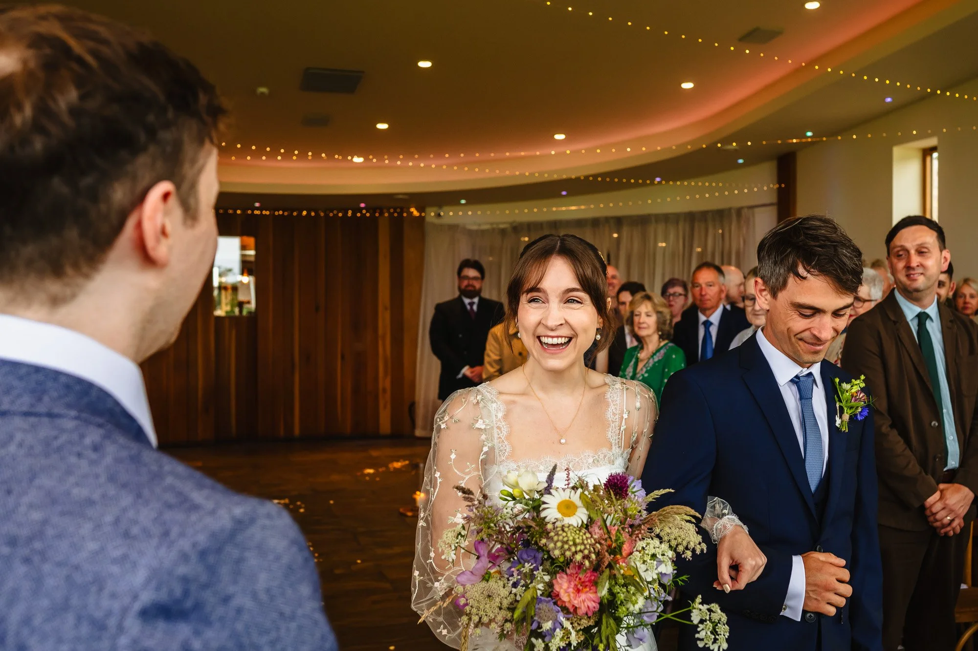 photograph of a bride walking down the aisle towards her groom at the Out Barn in Lancashire by documentary wedding photographer Caroline Goosey