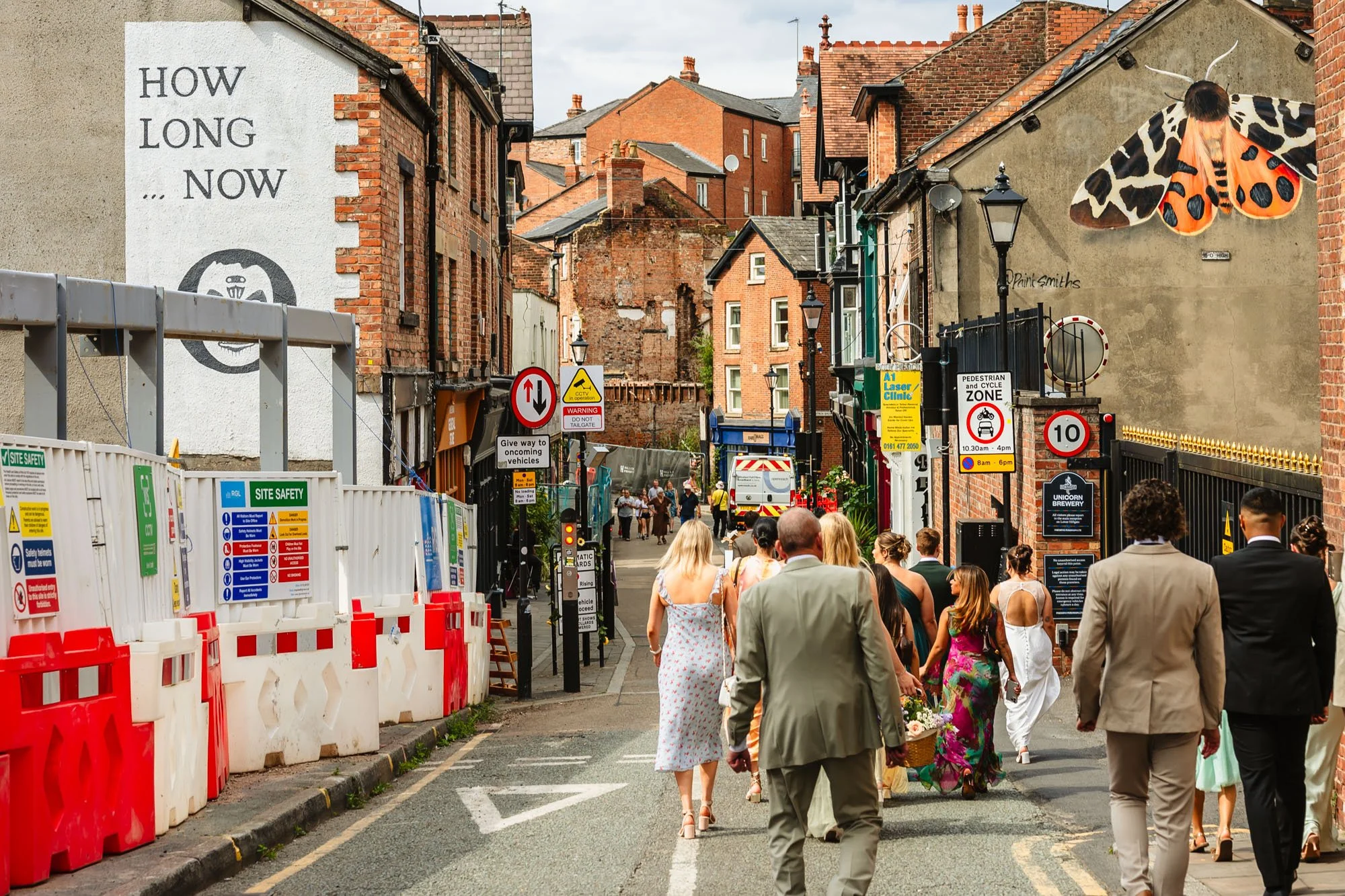 Photograph of a wedding party walking through Stockport town centre, surrounded by road signs, with murals on nearby walls.