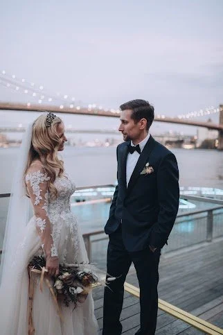 Bride and groom standing outdoors near a bridge at sunset