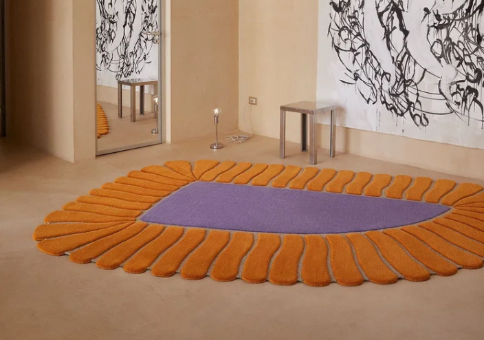 The M'Ama Non M'Ama rug by Patricia Urquiola features a lavender oval center with radiating orange petals arranged in a flower-like pattern.