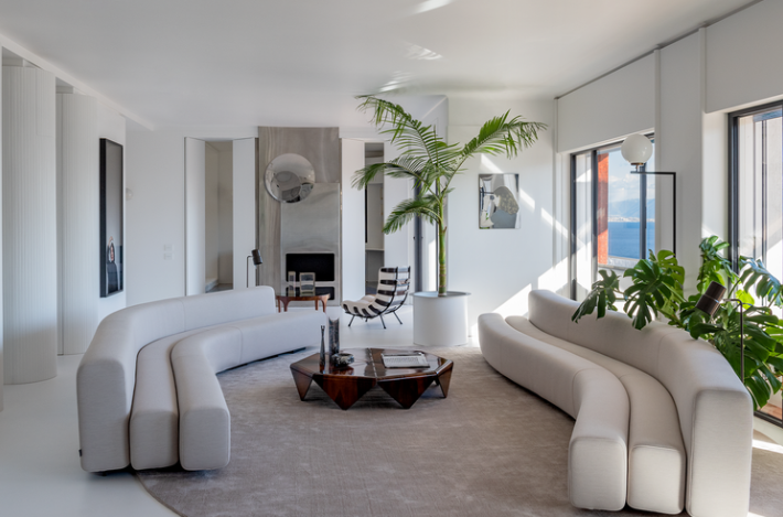 Osaka modular sofas featuring serpentine curved designs with off-white fabric upholstery, arranged around a geometric wooden coffee table in a spacious living room.