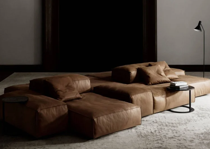 Extrasoft modular sectional sofa in brown leather featuring an ultra-low profile with oversized cushions and a relaxed, casual design on a light textured rug in a minimalist room.