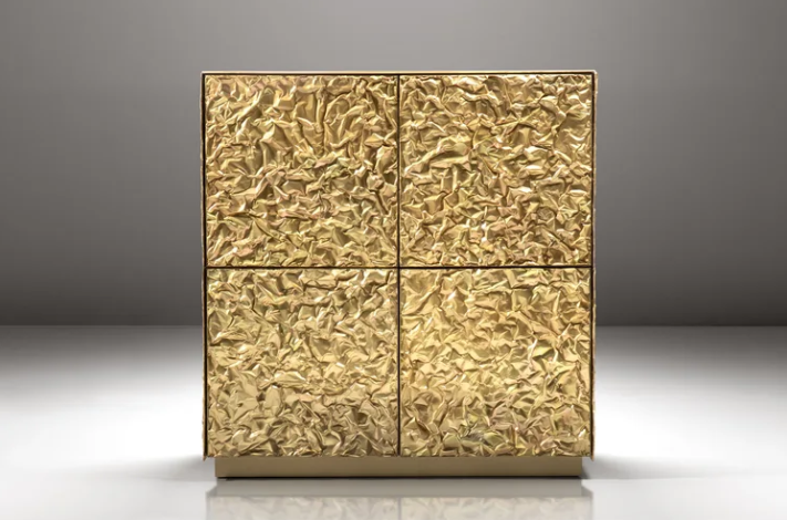 Froissé cabinet featuring a sculptural, crinkled metallic gold leaf finish across its four doors, set against a neutral gray background.