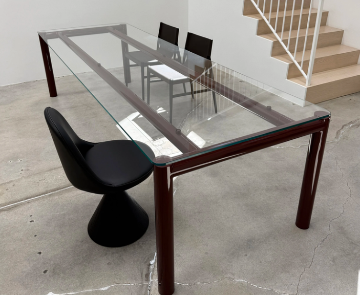 Ventiquattro dining table featuring a transparent glass rectangular top supported by a dark reddish-brown tubular frame, styled with modern black chairs.