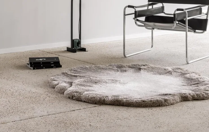 Stylish MSHWY01 area rug featuring an organic, cloud-like shape and plush light gray pile, styled on a polished concrete floor alongside a modern chrome armchair.