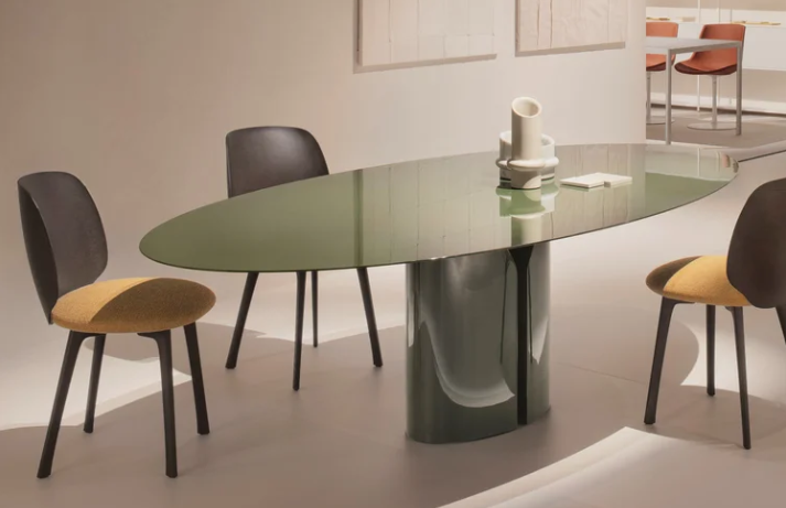Modern NVL table featuring an oval glossy sage green tabletop supported by two sculptural central bases with a matching glossy finish, styled with two-tone dining chairs.