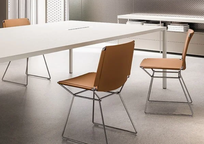 Tense dining table featuring a minimalist large white rectangular top with slim corner legs, styled with tan leather side chairs on wire frames.