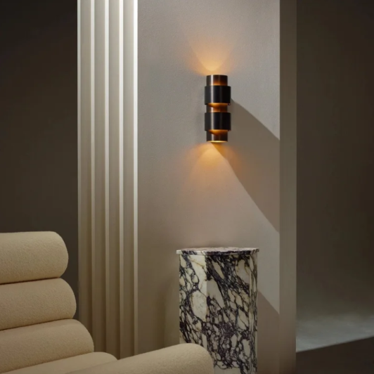 Ring wall lamp by CTO Lighting with cylindrical brass design creating a warm ambient glow in a refined bedroom interior.