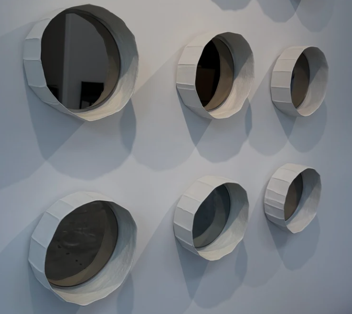 Modern Ninfea mirrors featuring round reflective glass enclosed in white fabric-covered cylindrical frames, arranged in a grid installation on a plain wall.