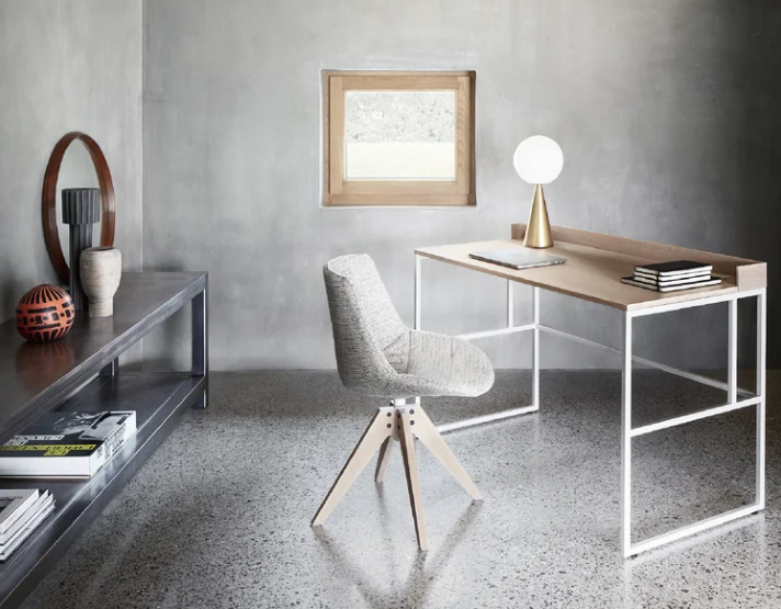 Flow chair displaying a light gray upholstered shell atop a four-star wooden swivel base, styled beside a minimalist wooden desk in a contemporary office setting.