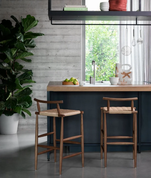 Pelleossa bar stools featuring natural wood frames with woven rattan seats and curved backrests, positioned at a navy blue kitchen island with a wood countertop in a modern kitchen setting.