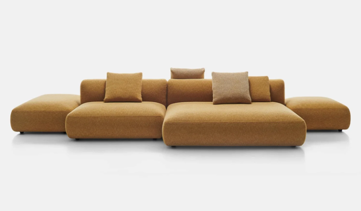 Cosy Island sofa featuring low-profile modular seating upholstered in textured mustard-yellow fabric with coordinating throw pillows and side ottomans.
