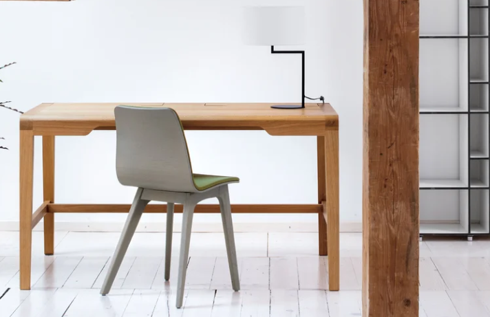 Secret wooden desk featuring a light oak top with integrated storage flaps and clean-lined legs, paired with a grey chair and a sleek black desk lamp.