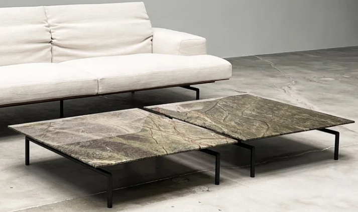 Sumo low coffee tables featuring square green-veined marble tops supported by slim black metal frames, styled next to a cream fabric sofa on a polished concrete floor.