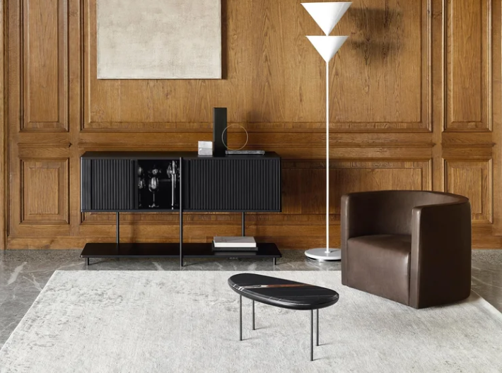 Pebble accent table that features an organic pebble-shaped black tabletop on slender metal legs, styled on a light rug alongside a leather armchair.