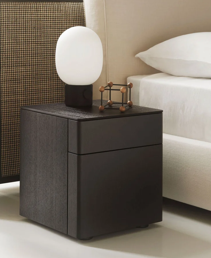 Byron nightstand by Piero Lissoni with rounded edges, an ash wood frame, and refined detailing beside an upholstered bed.